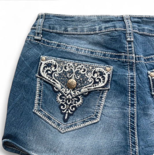 Close-up of blue denim shorts with decorative lace pocket on a white background